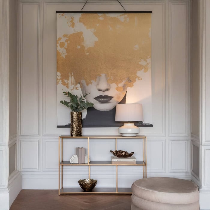 Stylish hallway with a large gold-accent artwork above a slim console table, decorated with a lamp, books, and a textured vase.