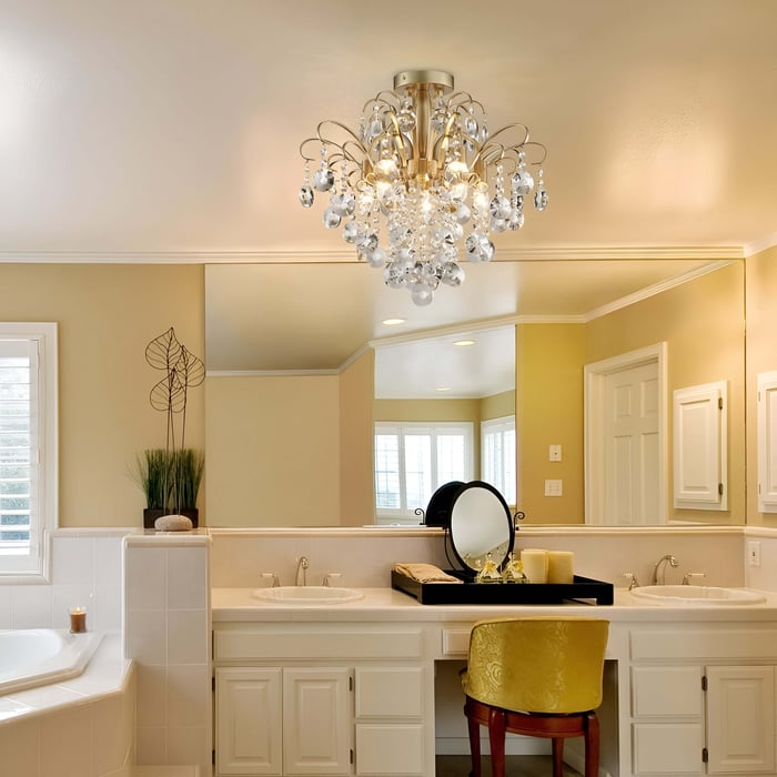 Warm bathroom vanity with crystal flush mount chandelier, dual sinks, and a golden velvet chair under soft lighting.