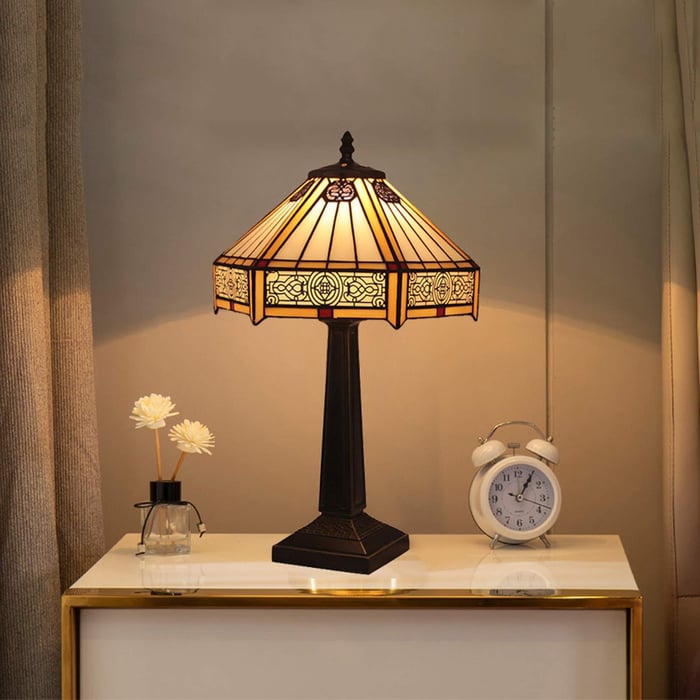 Classic Tiffany-style table lamp with ornate shade on a nightstand beside an alarm clock and decorative flowers