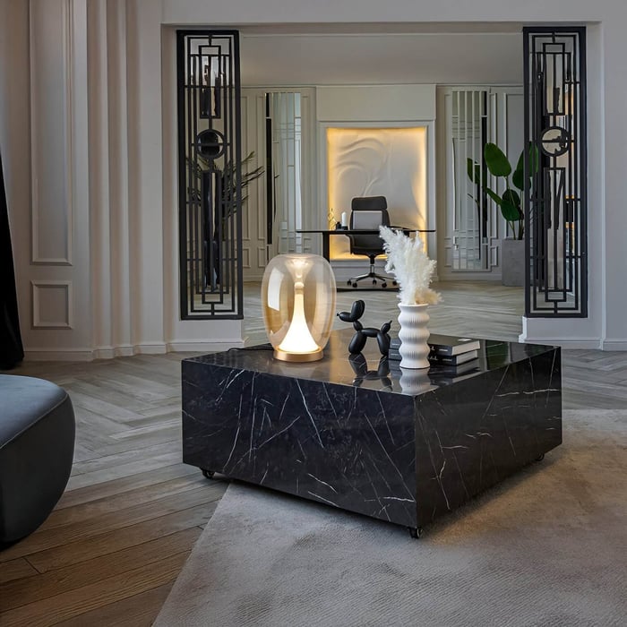 Sophisticated black marble coffee table with a glass dome lamp, books, and ceramic decor in a luxurious interior.