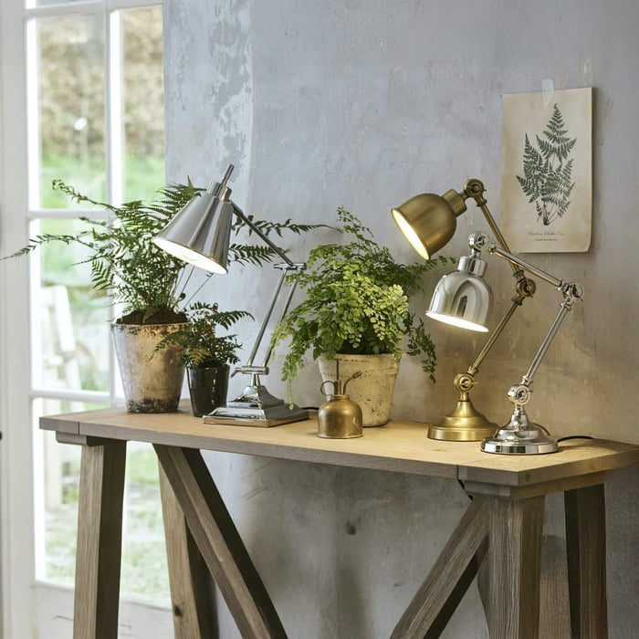 Trio of adjustable industrial desk lamps in silver, brass, and chrome on a rustic wooden console.