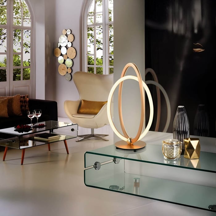 Modern living room with a glass coffee table featuring a sculptural LED lamp, decorative objects, and bold wall art.