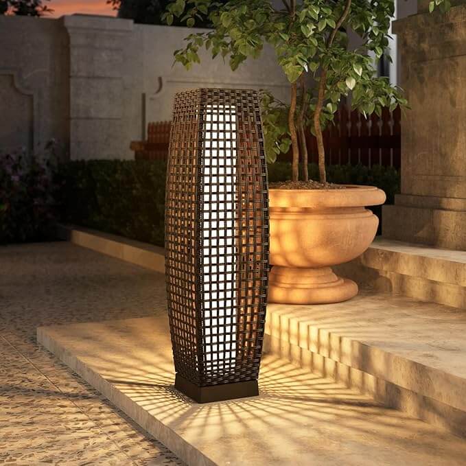 Tall woven outdoor lantern lamp casting patterned light beside stone steps and a large planter.