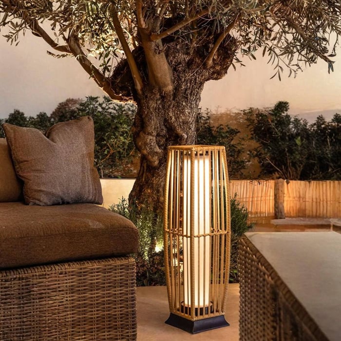 Rattan outdoor lantern floor lamp beside a sofa near a tree, creating warm poolside ambience.