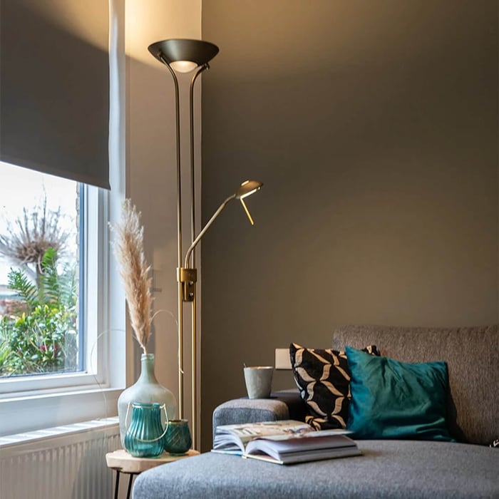 Cozy living room nook with a dual-head brass floor lamp, teal glass decor, and a magazine open on the grey sofa.