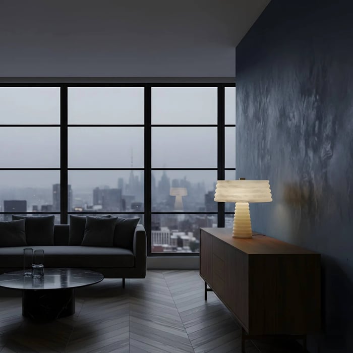 Contemporary apartment living room at dusk with dark blue accent wall and panoramic city windows, featuring a sculptural white table lamp on a wooden sideboard beside a sofa and round coffee table.