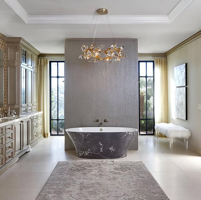 Spa-like bathroom with statement chandelier, freestanding floral bathtub, large windows, and elegant beige cabinetry.