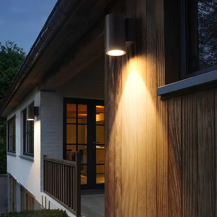 Modern wall sconce casting warm light on wood siding at dusk.