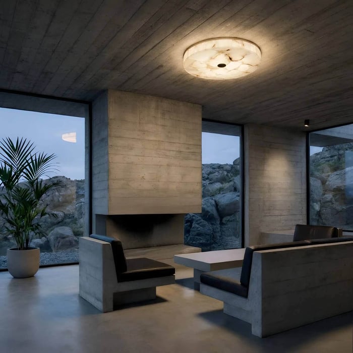 Minimalist concrete living space with large floor-to-ceiling windows overlooking rocky terrain, featuring a round flush-mount ceiling light and built-in seating around a fireplace.