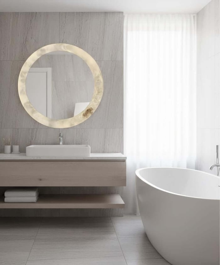 Luxury bathroom with round alabaster mirror above vanity beside freestanding bathtub.