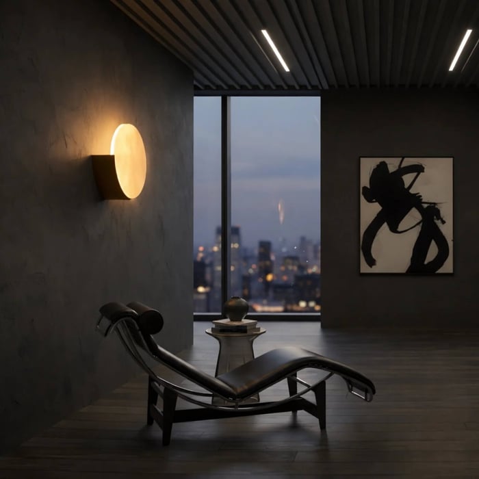 Modern lounge with a sculptural chaise longue and city view at dusk, highlighted by a round wall-mounted light on a dark textured wall.