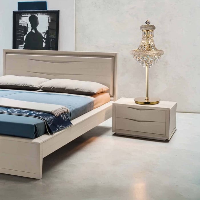 Gold crystal chandelier-style table lamp on a bedside cabinet next to a modern bed in a neutral bedroom.