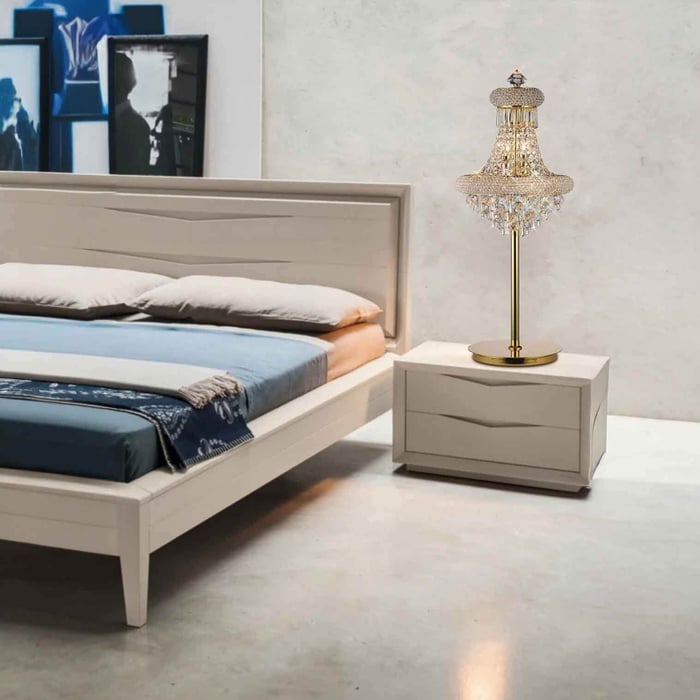Gold-based crystal table lamp beside a light grey bed with blue bedding in a modern bedroom.