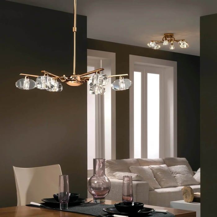 Gold chandelier with clear glass shades hanging above a modern dining table in an open-plan living room.