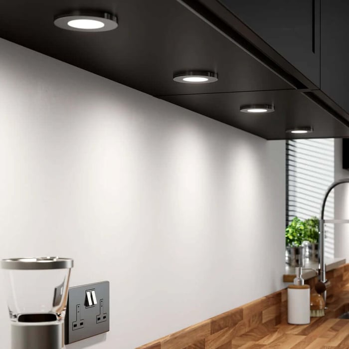 Black under-cabinet lighting puck lights creating soft pools of light across a kitchen backsplash and counter.
