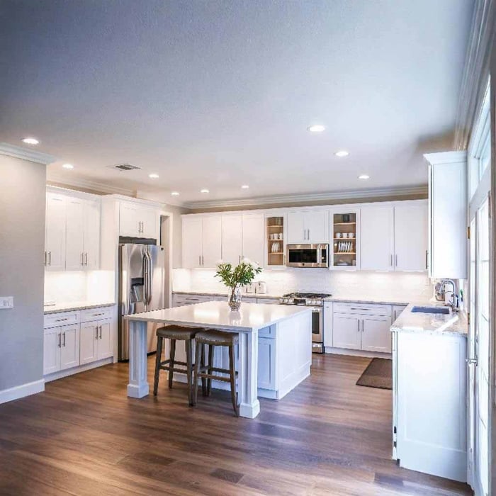 Classic white kitchen with a central island, evenly spaced recessed downlights, and bright, clean overall illumination.