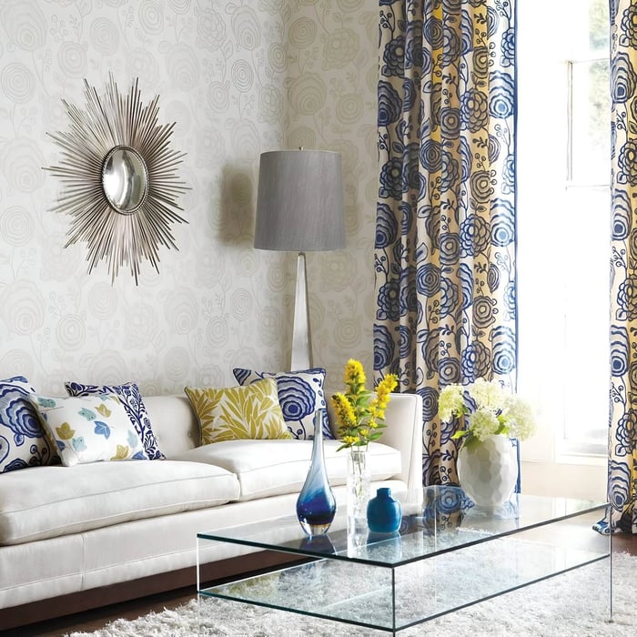 Metallic floor lamp with grey shade placed beside a white sofa in a vibrant living room with floral curtains and glass table.