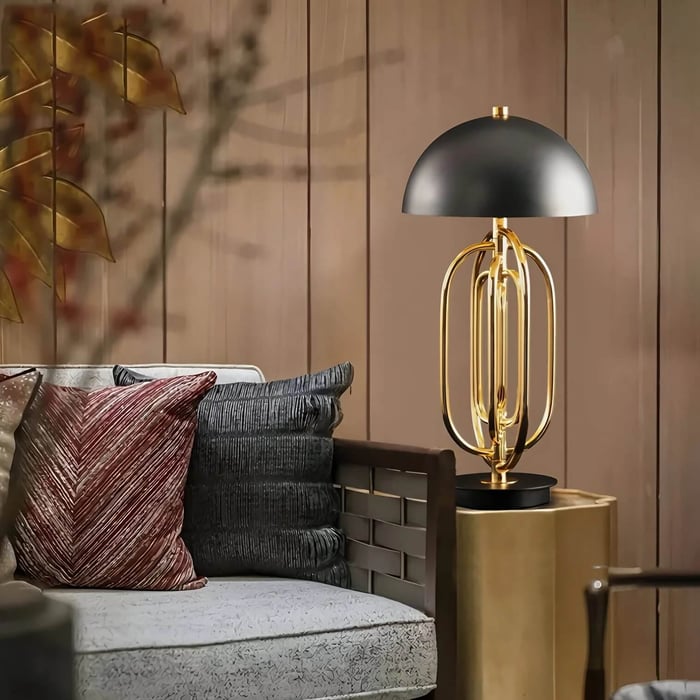 Black dome table lamp with a gold sculptural base on a side table beside a sofa in a warm-toned living room.