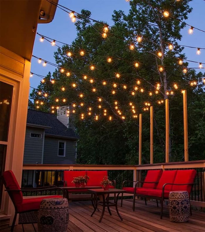 Outdoor string lights strung in a canopy above a wooden deck with red patio seating at dusk.
