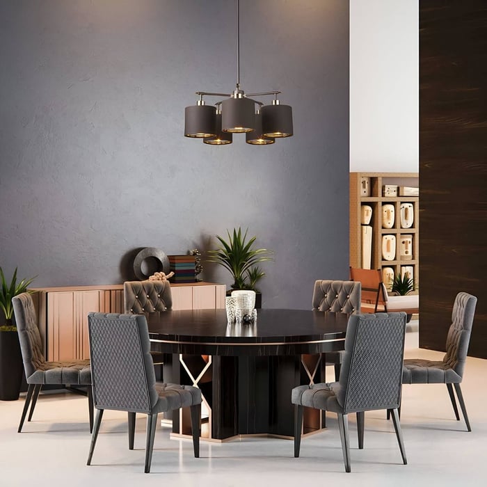 Modern dining room with a round black table, six tufted grey chairs, and a ceiling fixture of five matte black chandelier lights with gold interiors.
