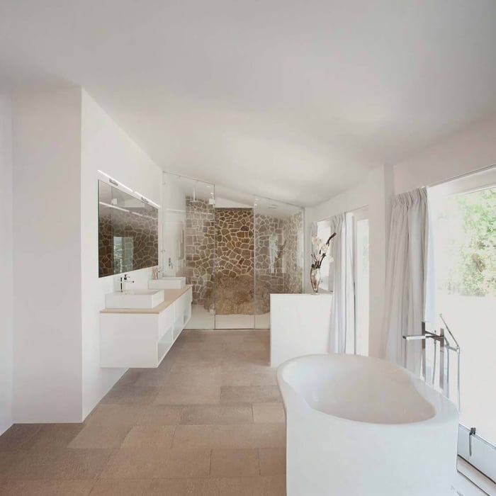 Airy spa-like bathroom with a floating double vanity, glass shower enclosure with a stone feature wall, and a freestanding tub near large windows.