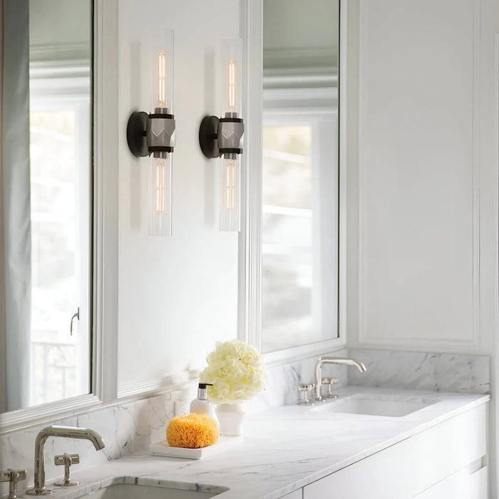 Close-up of a white vanity area with a marble countertop, two modern wall sconces beside a mirror, and a vase on the counter.
