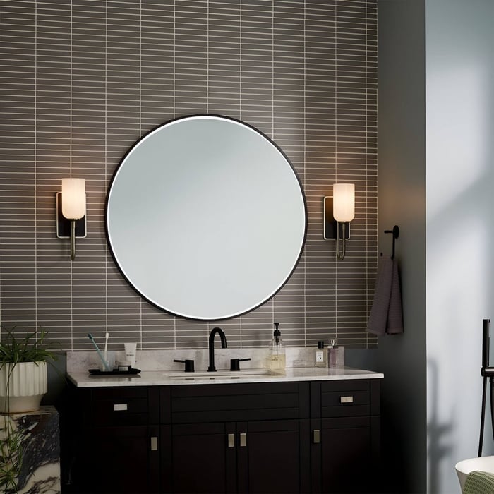 Modern bathroom vanity with dark cabinetry, a large round backlit mirror, and two sleek wall sconces with frosted shades.