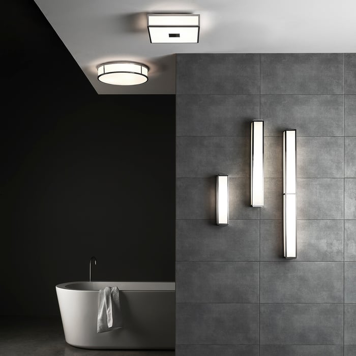 The image depicts a modern bathroom with sleek lighting, including a freestanding bathtub, ceiling-mounted lights, and vertical wall sconces. The minimalist design, paired with neutral-toned tiles, creates a refined, luxurious ambiance.