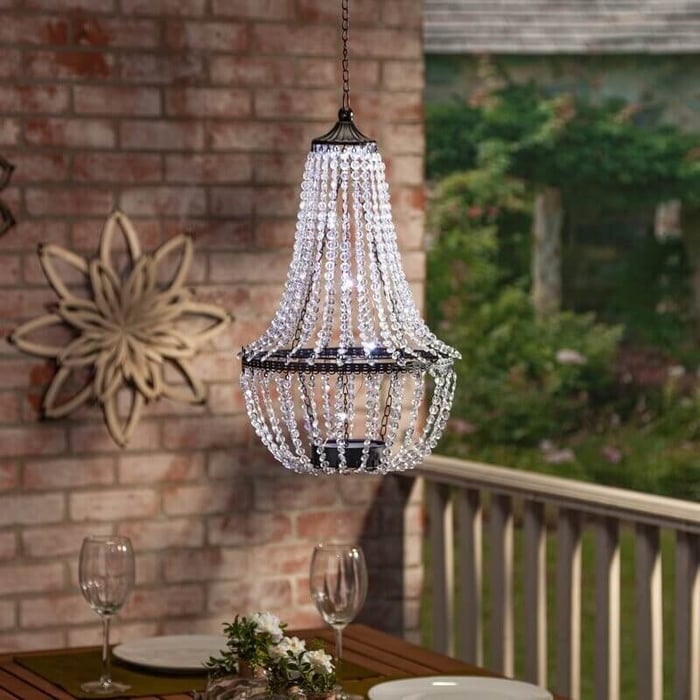 Beaded outdoor chandelier hanging over a small patio table on a covered porch with brick wall backdrop.