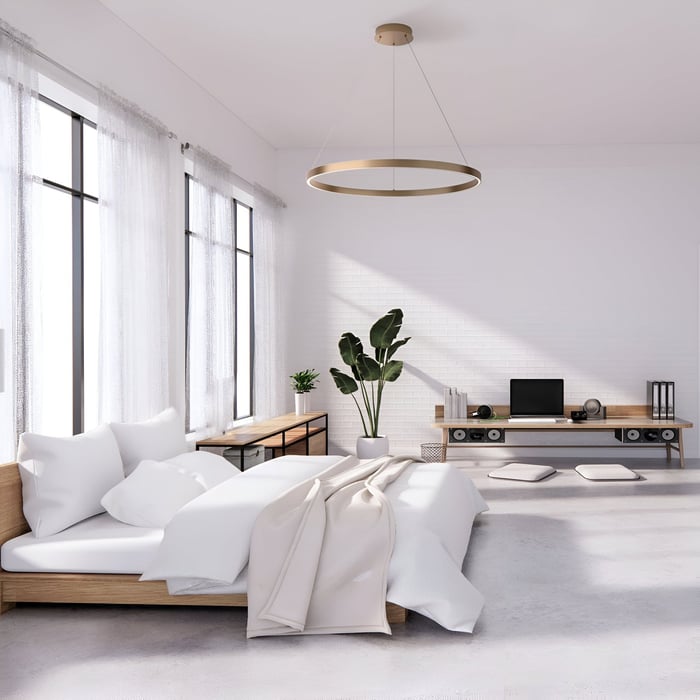 Bright minimalist bedroom with a circular gold pendant and white, airy furnishings.