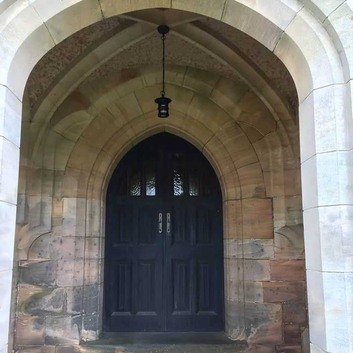 Stone arch doorway with a single black hanging pendant light centred above double doors.