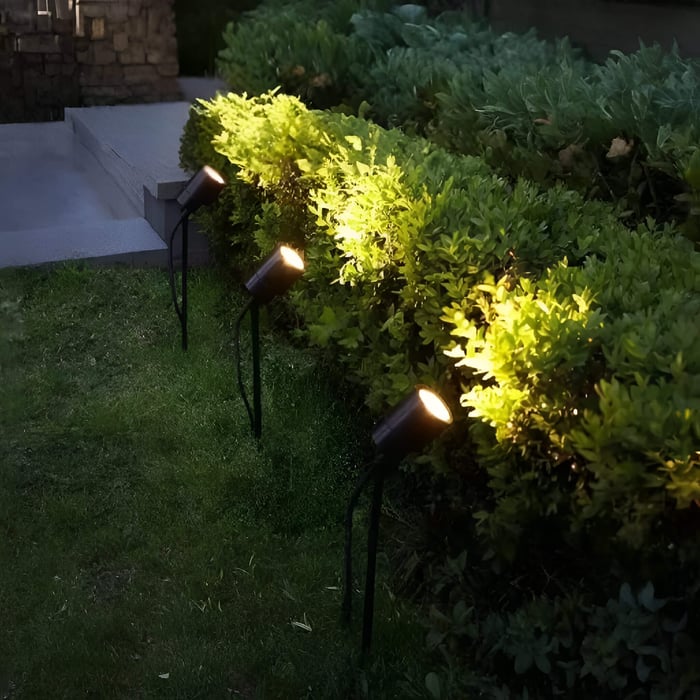 Row of garden spike spotlights lighting up a hedge beside stone steps.
