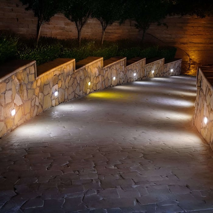 Curved stone driveway at night with recessed wall lights casting bright pools of light along both sides of the path.