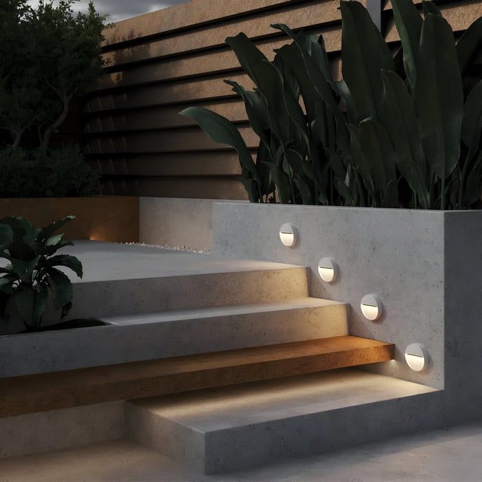 Modern outdoor steps illuminated with round recessed wall lights, featuring concrete planters, lush green plants, and a sleek contemporary exterior design.