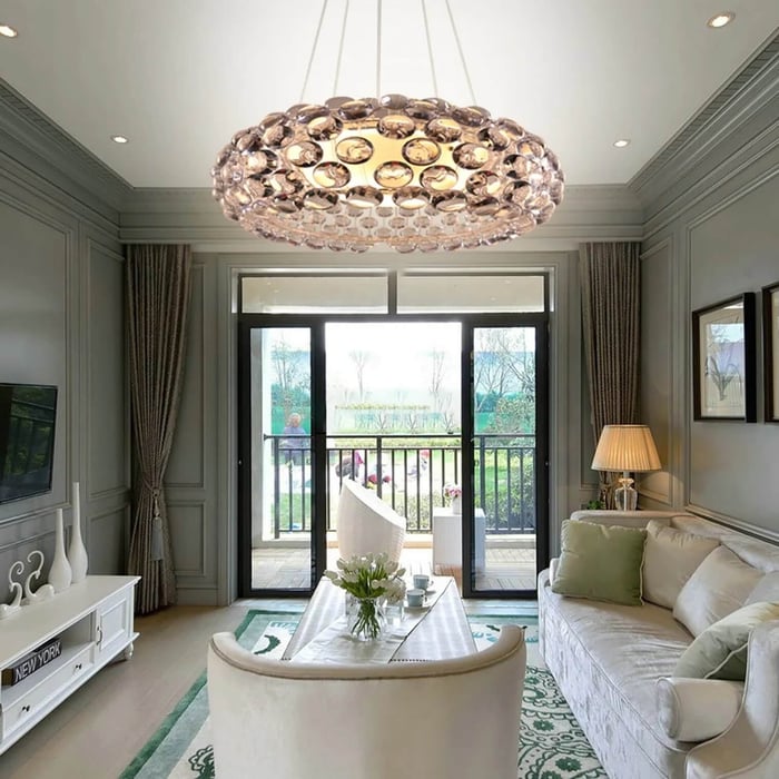 Oversized round crystal disc chandelier suspended in a classic lounge with paneled walls and a view through glass doors.