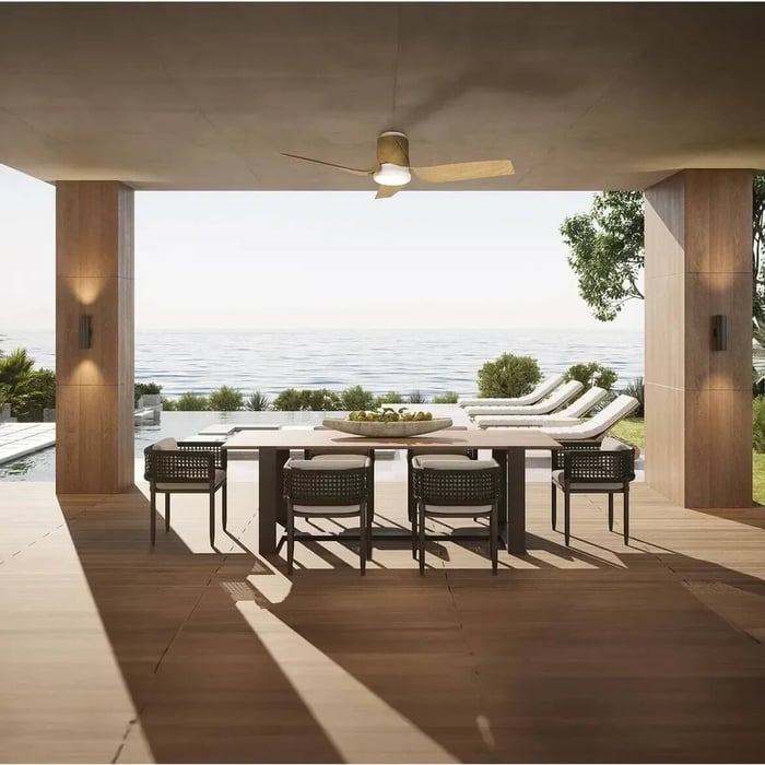 Outdoor dining terrace with wooden ceiling fan light above a large table, overlooking a pool and sun loungers facing the sea.