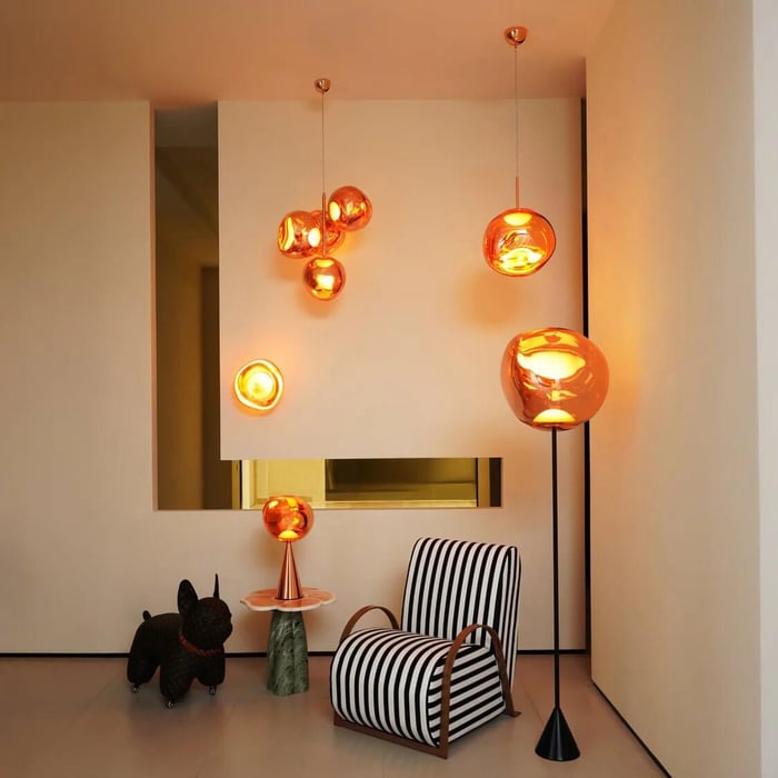 Modern room with warm amber glass globe lights pendant, wall, table, and floor glowing beside a black-and-white striped lounge chair and a playful dog sculpture.