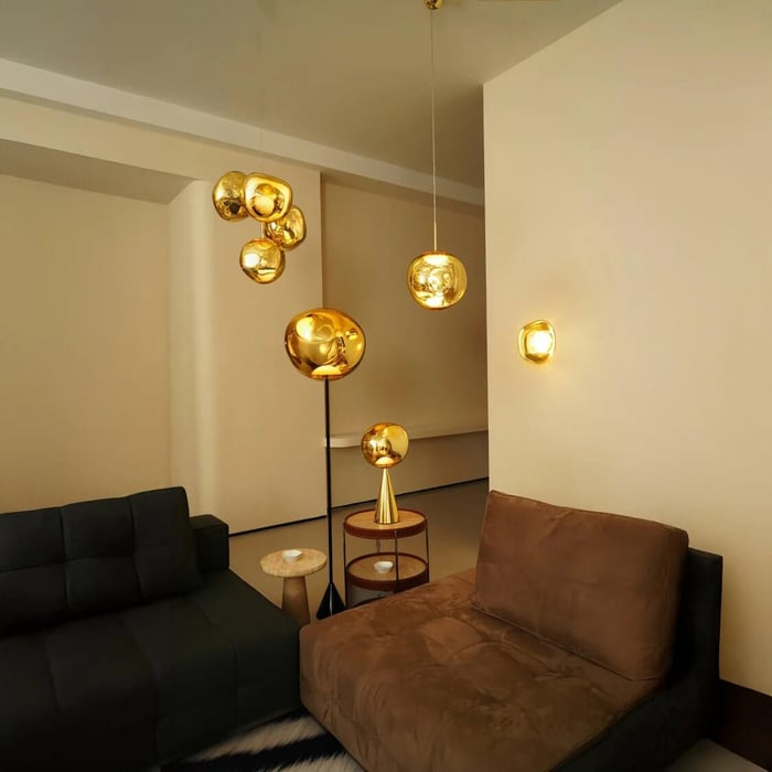 Contemporary living room with gold pendant and floor lights, dark sofa, brown lounge chair, and minimalist beige walls.