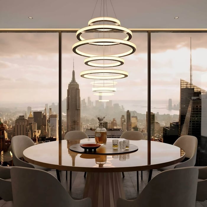 Modern multi-ring LED chandelier in a gold finish hanging above a round dining table with a city skyline view.
