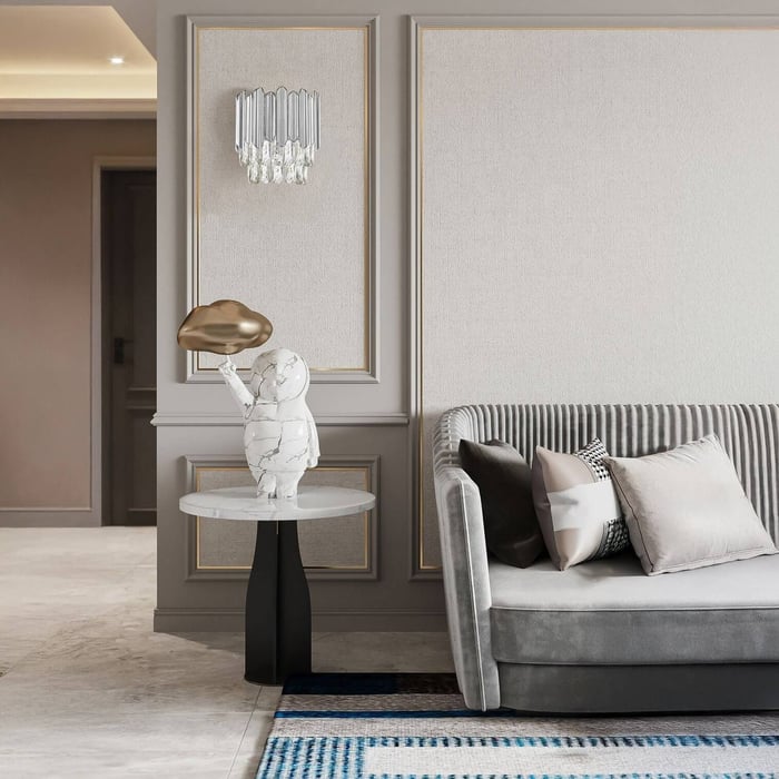 Elegant living space with a gray sofa, marble side table, sculptural lamp, and a crystal wall sconce on a paneled wall.