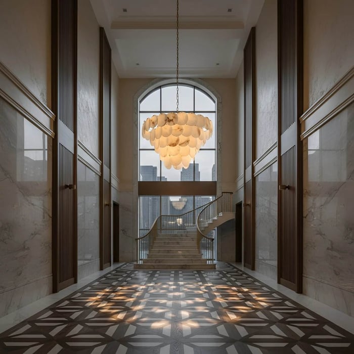 Grand marble foyer with a sweeping staircase and a large sculptural chandelier hanging beneath an arched window.