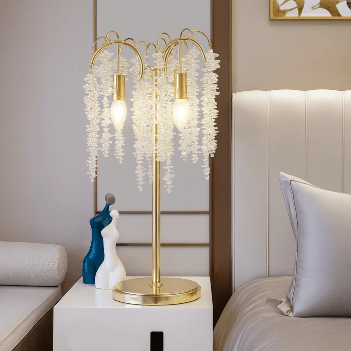 Gold blossom table lamp with cascading glass strands on a bedside table in a softly lit modern bedroom.