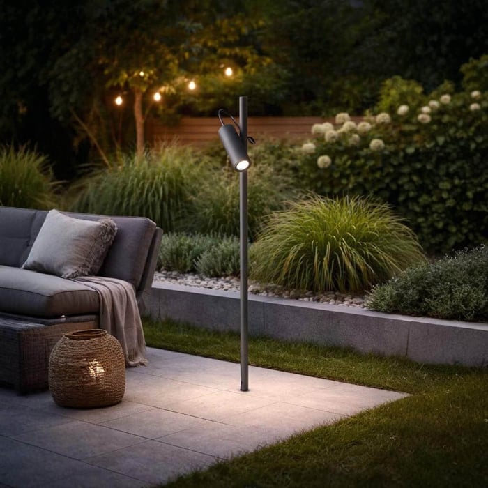 Minimal outdoor floor lamp with adjustable spotlight illuminating a patio beside outdoor seating and planting.