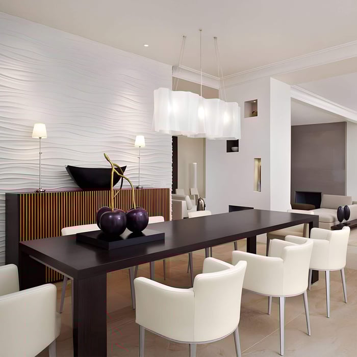Layered white fabric pendant lights above a black dining table surrounded by cream chairs in a textured white interior.