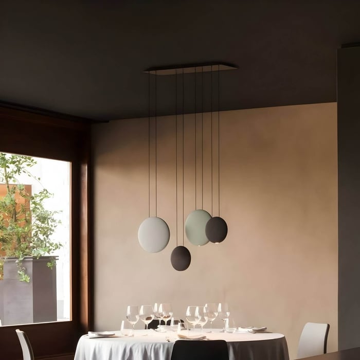 Minimalist dining setting with suspended circular pendants, round white table, and elegant place settings under soft ambient lighting.