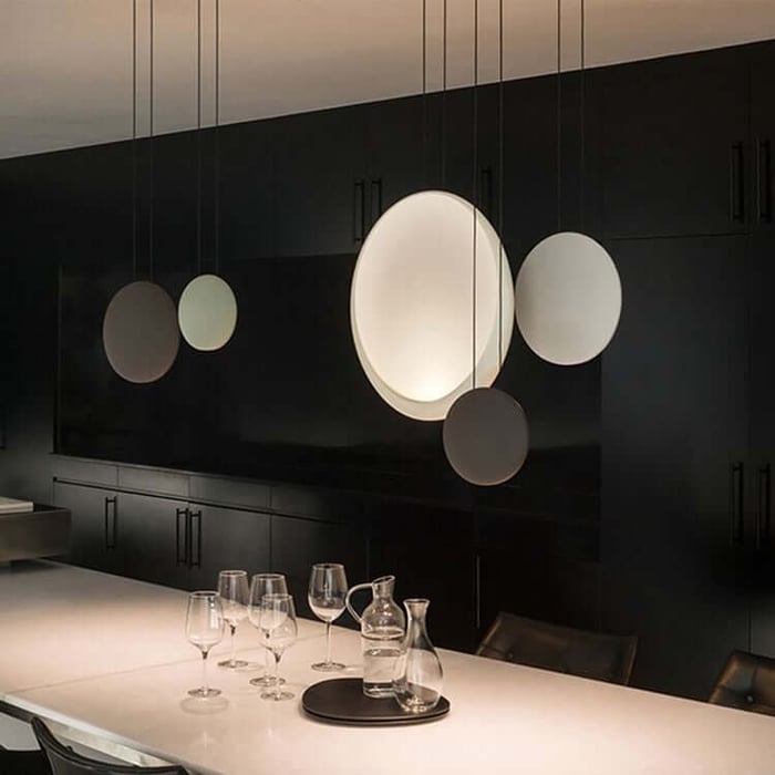 Minimalist dining space with artistic circular pendant lights and glassware on a light table.