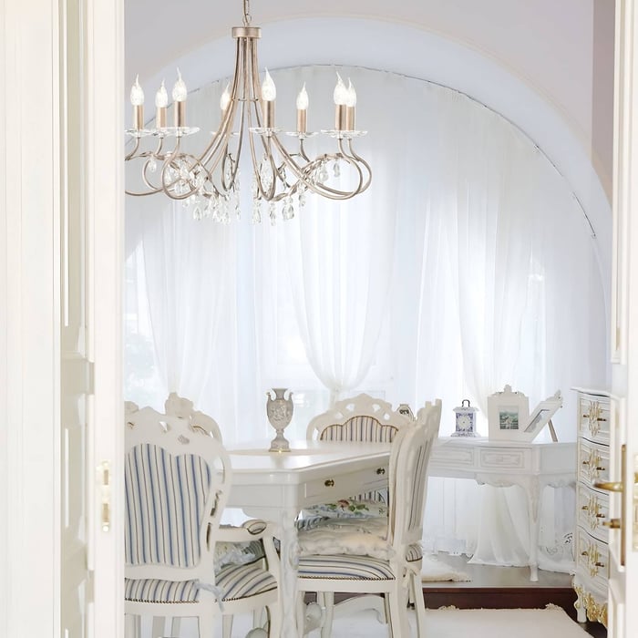 Bright white dining space with vintage furniture, striped upholstered chairs, and a chandelier with crystal accents under a curved window.