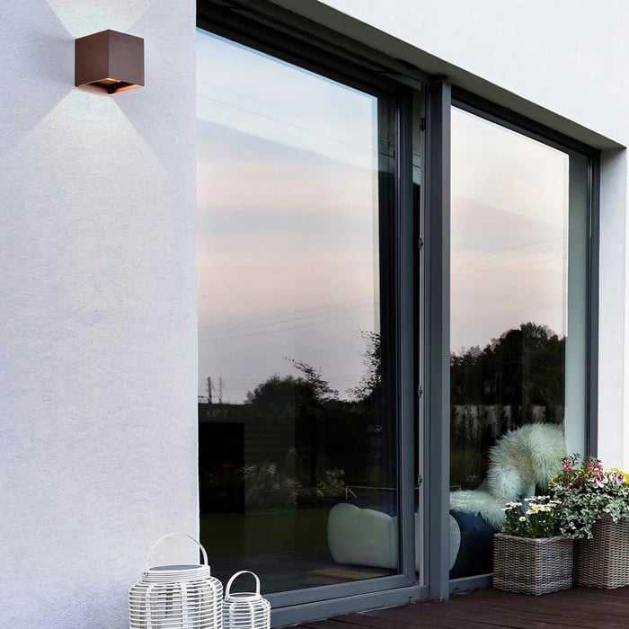 Minimalist white exterior with a small cube outdoor wall light beside large sliding glass doors overlooking a patio.
