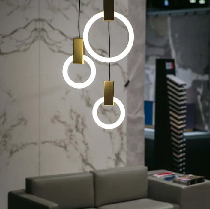 Modern living room with three circular LED ring pendant lights in front of a marble wall and grey sofa.