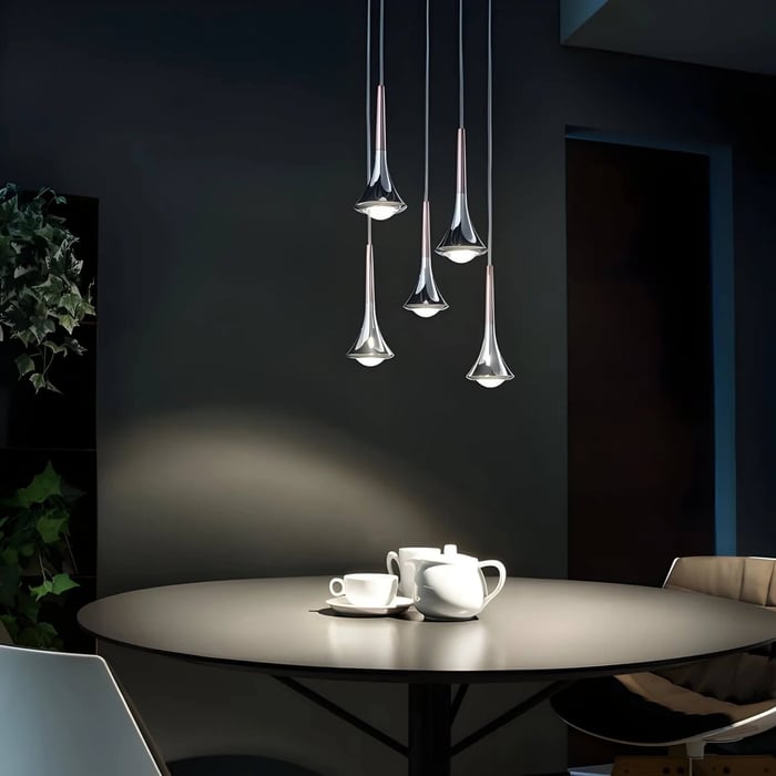 Moody dining space with five trumpet-shaped chrome pendant lights hanging above a round table set for tea.
